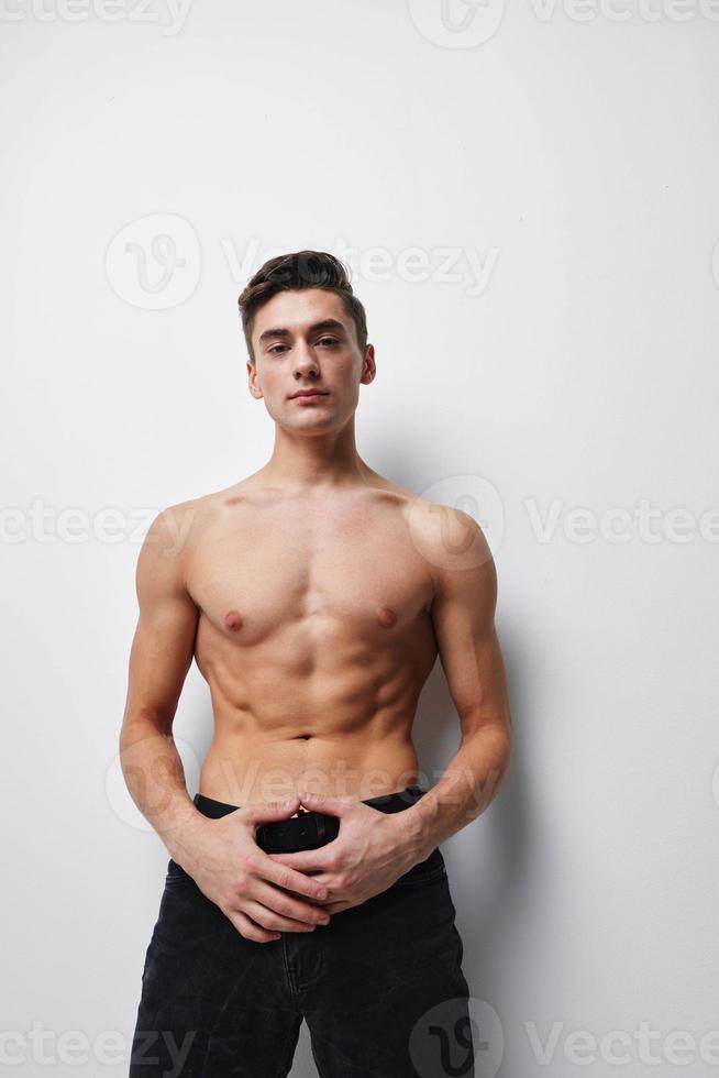 sexy semidesnudo chico sostiene pantalones con su manos en un ligero antecedentes foto