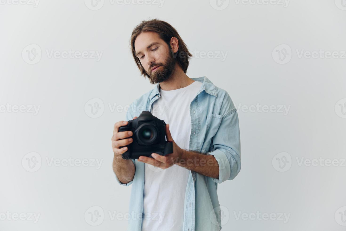 A male hipster photographer in a studio against a white background looks through the camera viewfinder and shoots shots with natural light from the window. Lifestyle work as a freelance photographer photo