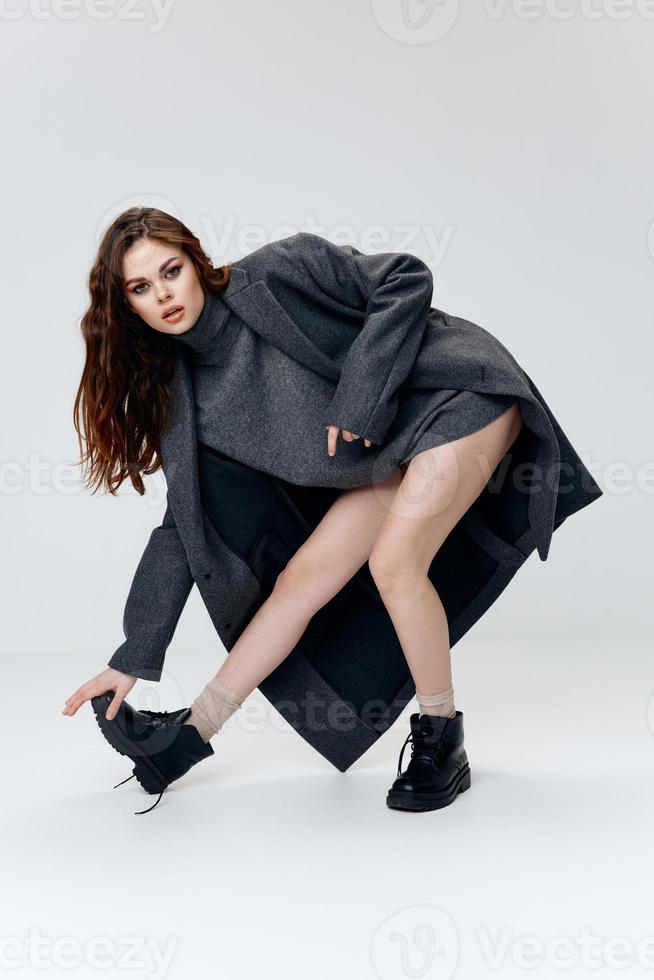 woman in a jacket and coat touches shoes with her hands on a light background in full growth photo