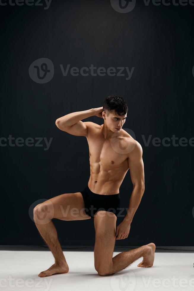 sexy man with naked muscular body kneels against a dark background photo
