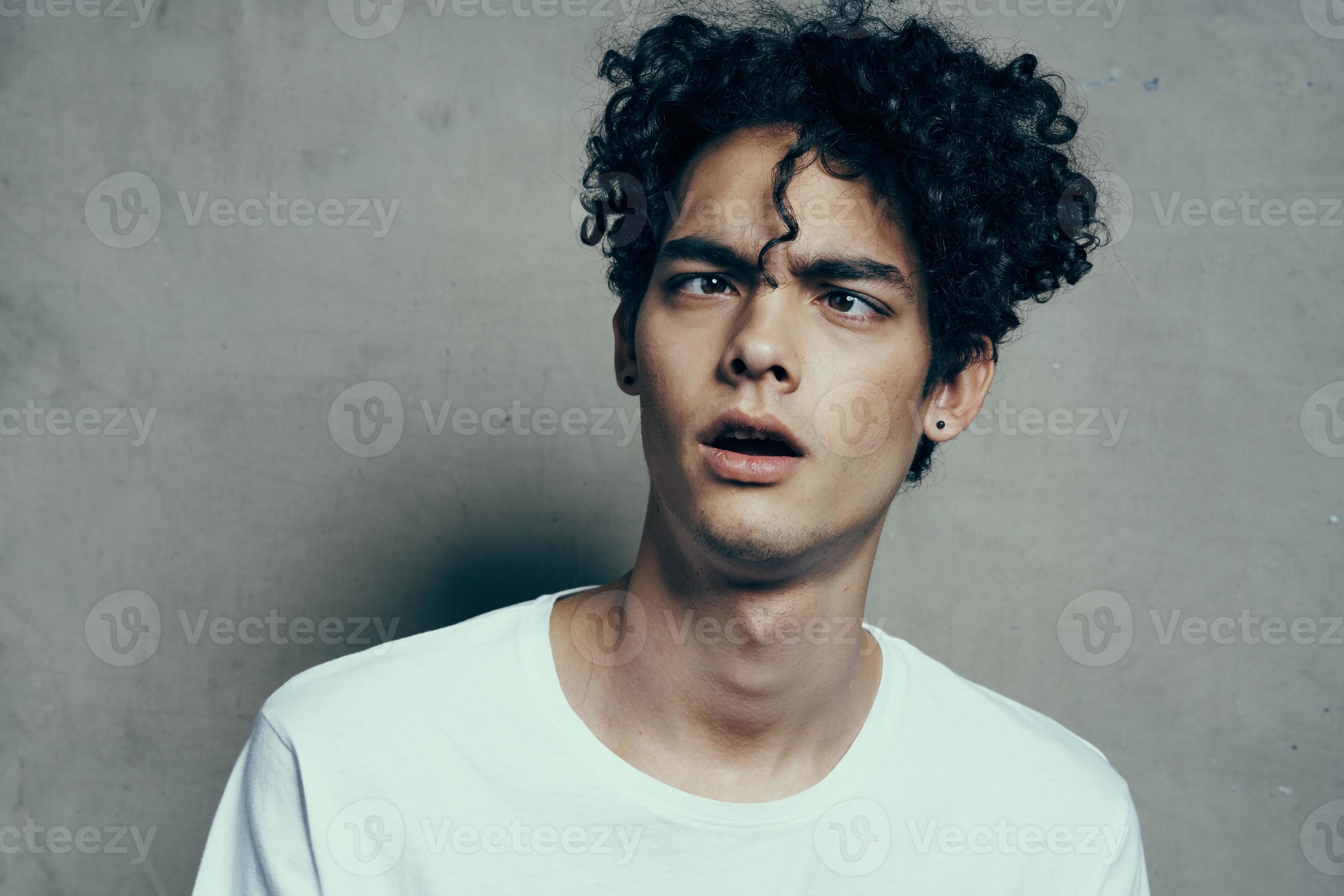 portrait of a handsome guy with curly hair on a gray background white t