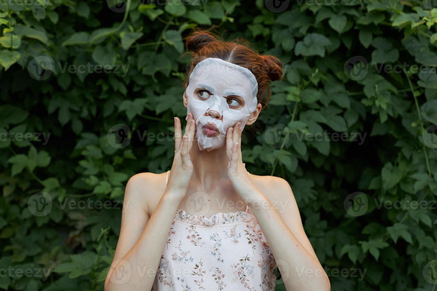 Beautiful woman white mask Touch your face with your hands bare shoulders bushes in the background photo