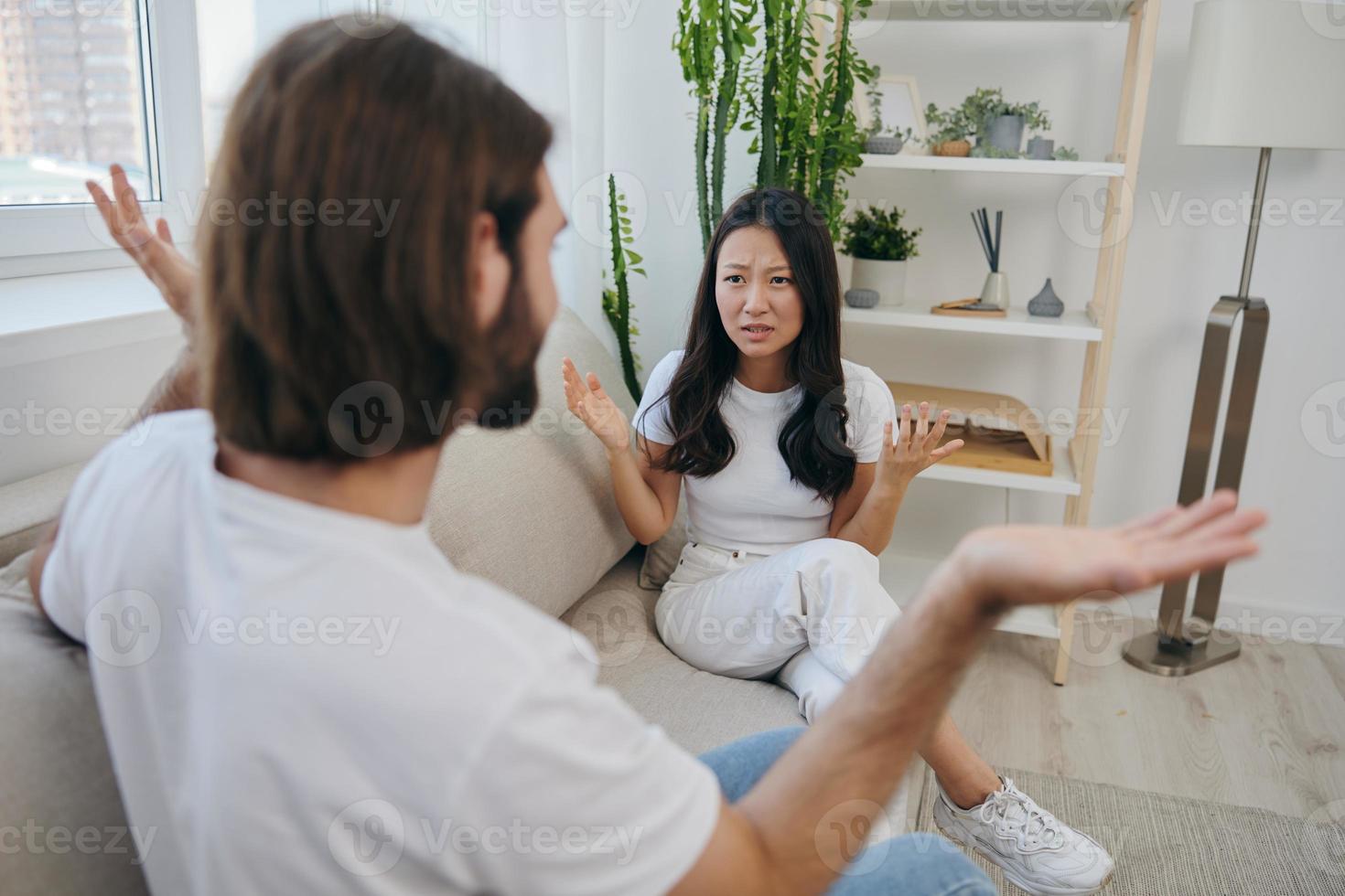 un hombre y un mujer sentar en el sofá a hogar en blanco camisetas y gritos comunicar escandalosamente hacer no entender cada otro. un pelea en el familia de dos esposos y agresión, triste emociones foto