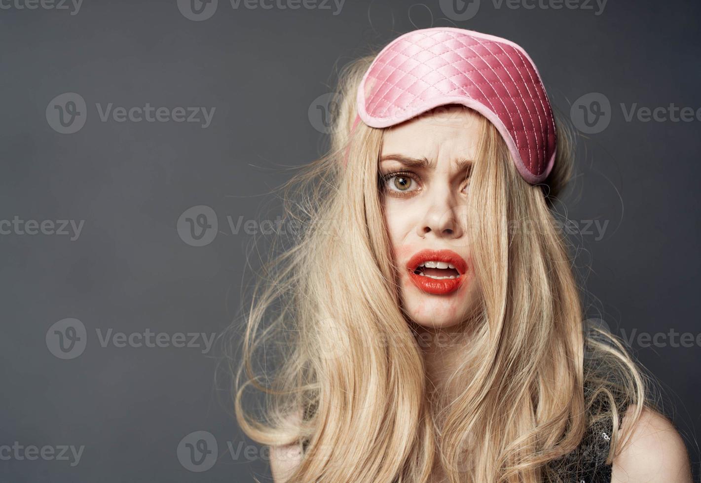 portrait of a blonde in a sleep mask and bright makeup lipstick smeared on her face photo