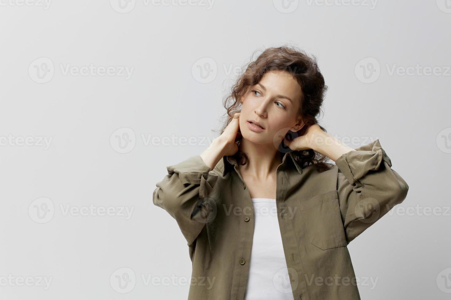 Pensive curly beautiful woman in casual khaki green shirt think about work problems cross hands behind head posing isolated on over white background. People Emotions Lifestyle concept. Copy space photo