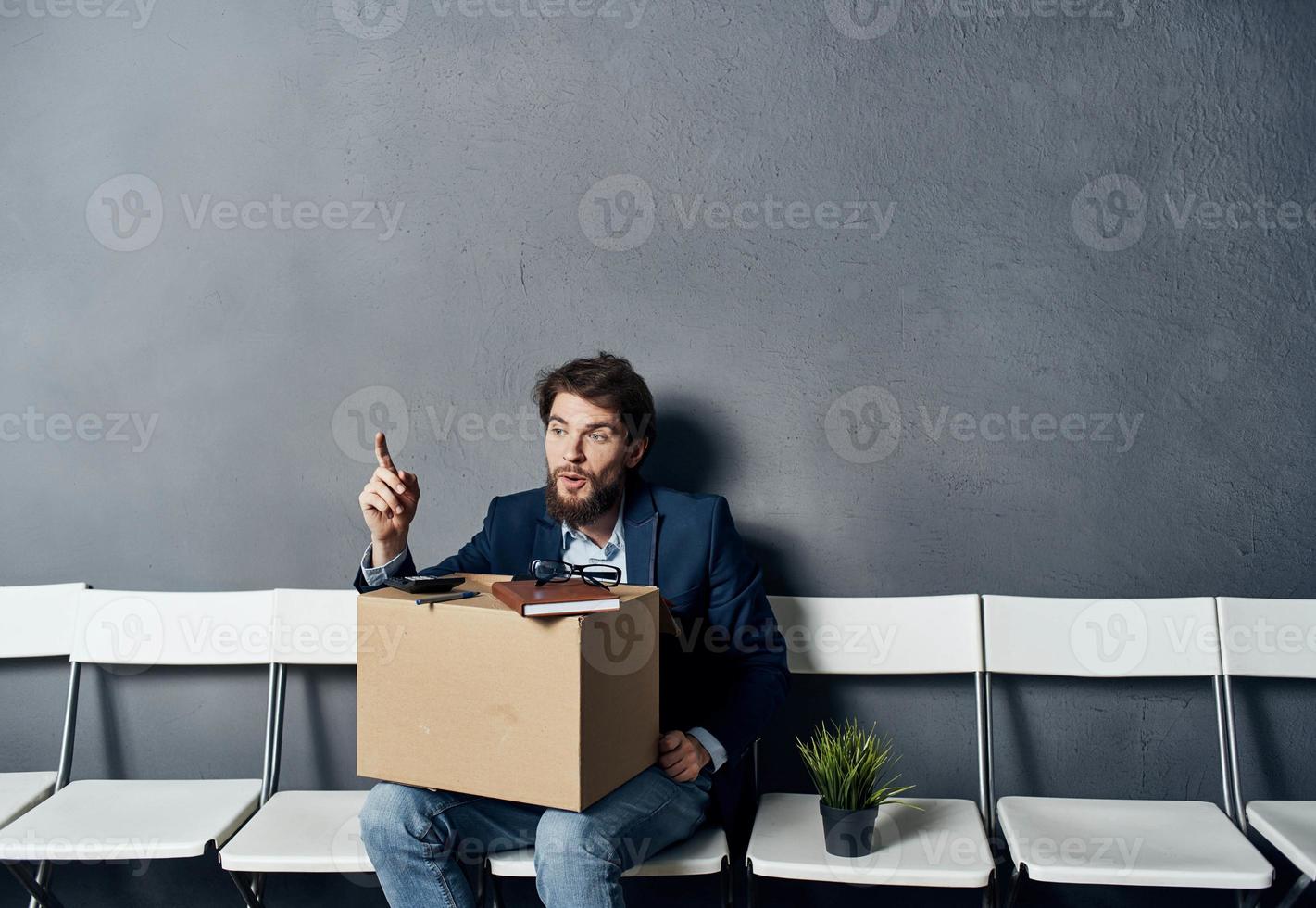 A man in a suit sits on a chair with a box job search depression photo