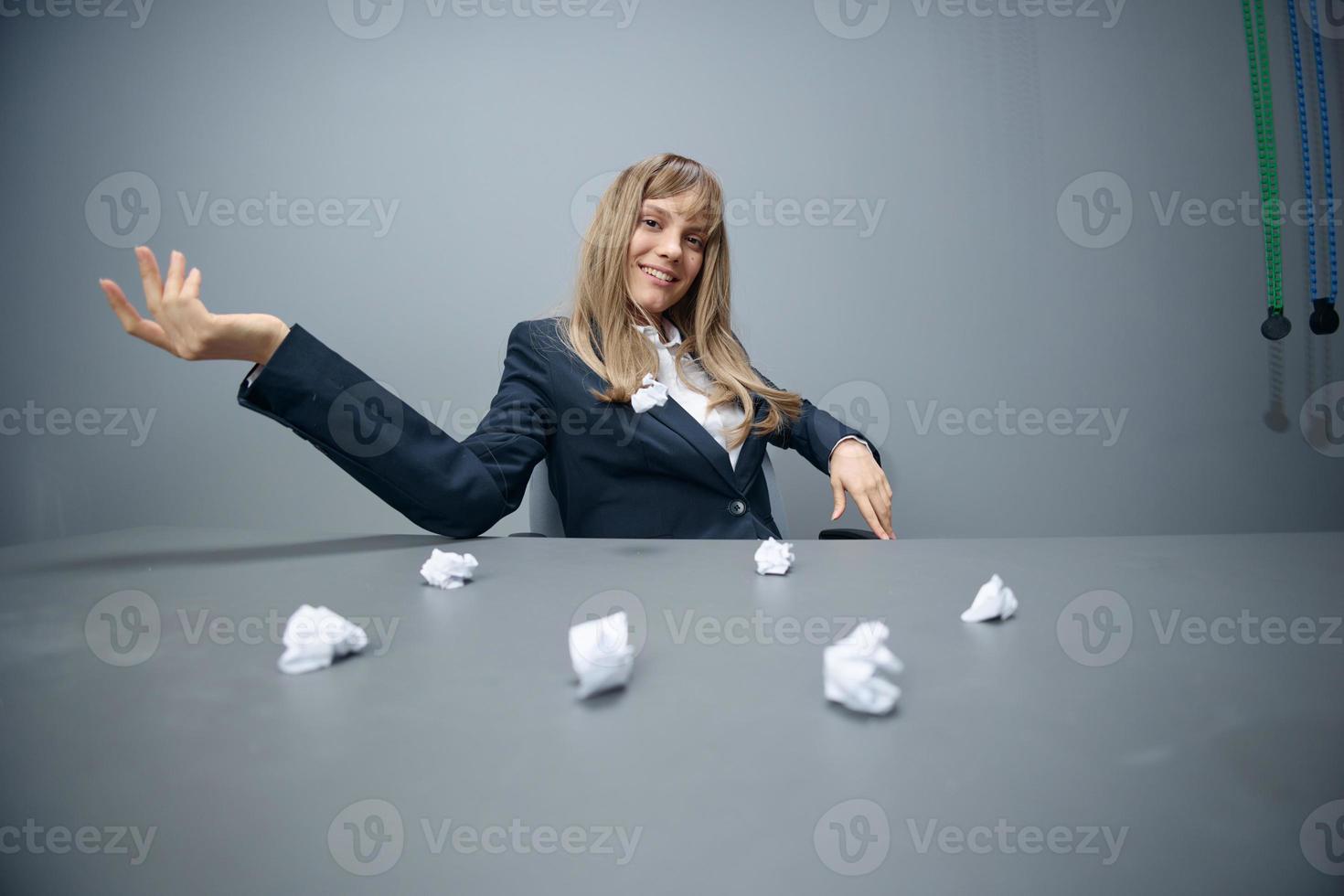 Pretty millennial blonde businesswoman worker in blue jacket throws papers into the camera sitting at workplace in gray modern office. Big boss Concept. Copy space, wide angle photo