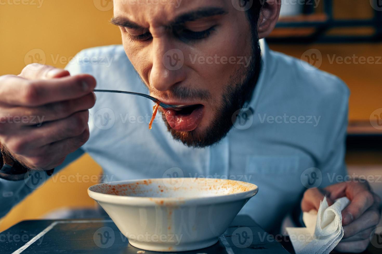 a handsome man with a beard eats borscht in a plate at a table in a cafe and a watch on his hand photo