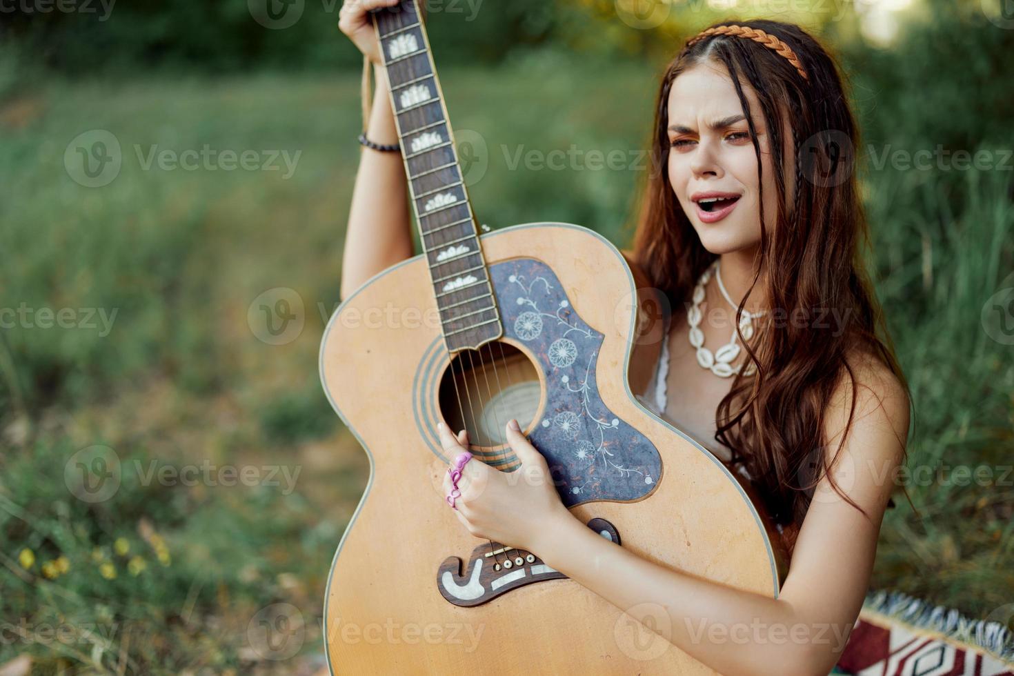 Beautiful woman playing guitar in nature in a hippie summer look, singing songs style of life without worries photo