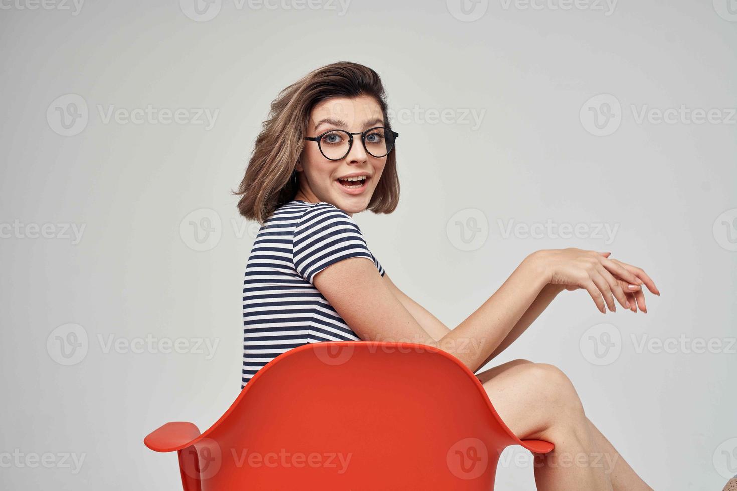 pretty woman in fashionable clothes sitting on the red chair posing Studio photo