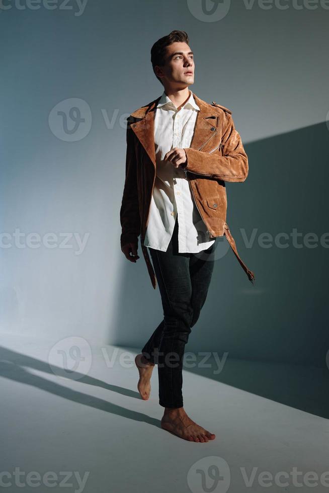 Fashionable man in a brown jacket on a gray background and a tilt in the form of shadows on the wall photo