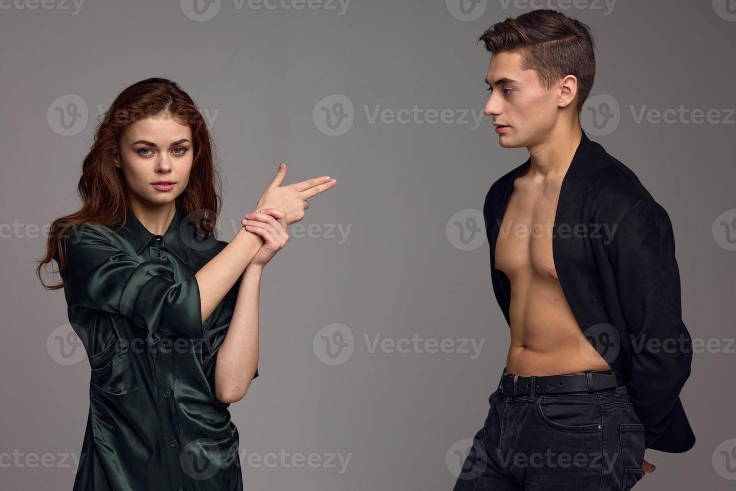 a woman shows two fingers to the side on a gray background and a man in an unbuttoned jacket photo