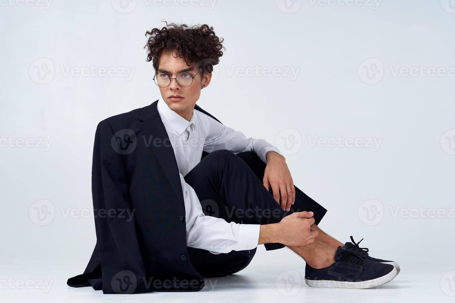 stylish man with curly hair in sneakers on a light background a jacket on the shoulder pants model photo