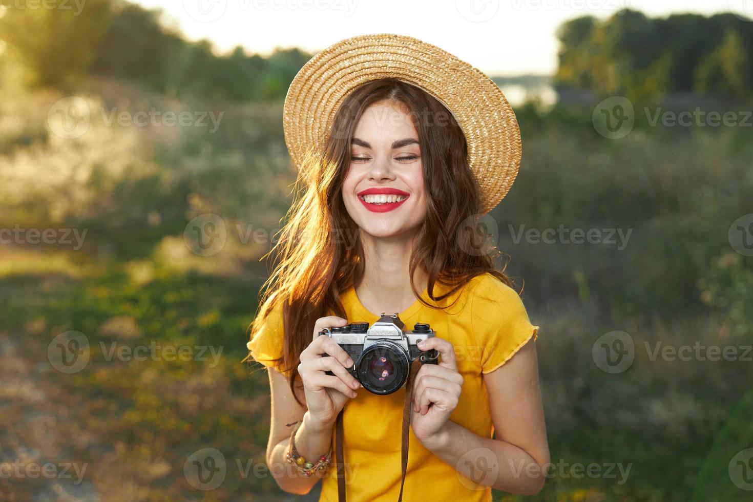 Smiling woman with closed eyes and with a camera in her hands in a hat on nature photo