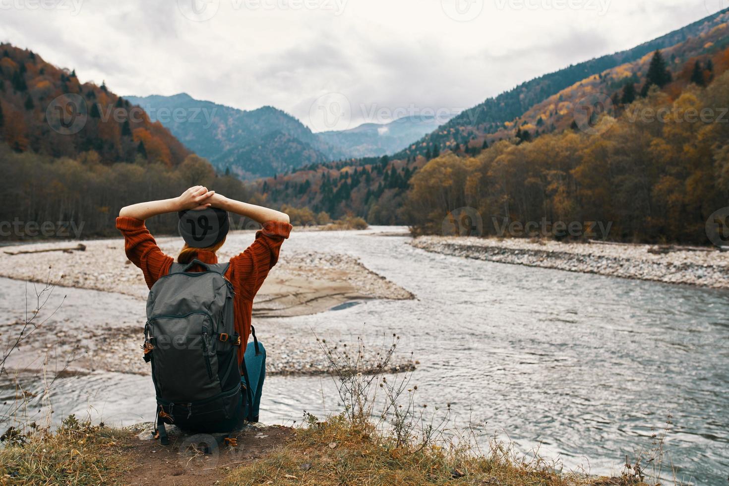 woman traveler with a backpack near the river on the grass and mountains in the distance photo
