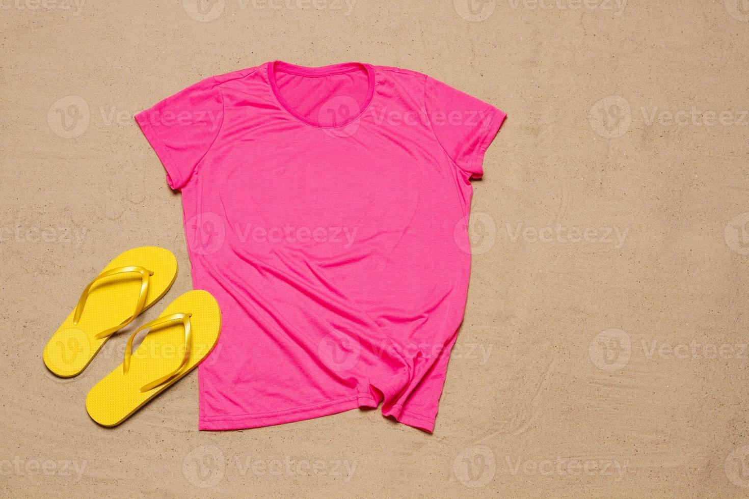 Sand beach texture background. Mockup pink summer t-shirt copy space. Blank template woman shirt Top view. Summertime accessories flip-flops. Flat-lay closeup tshirt on seashore. Beachtime photo