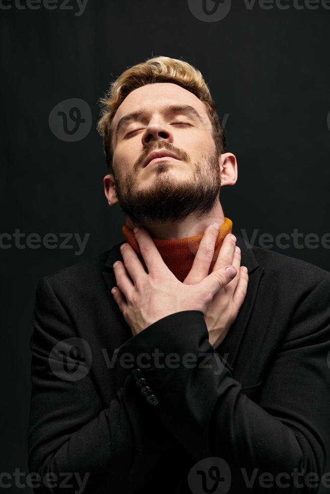 attractive blond man on a dark background in an orange sweater and coat photo