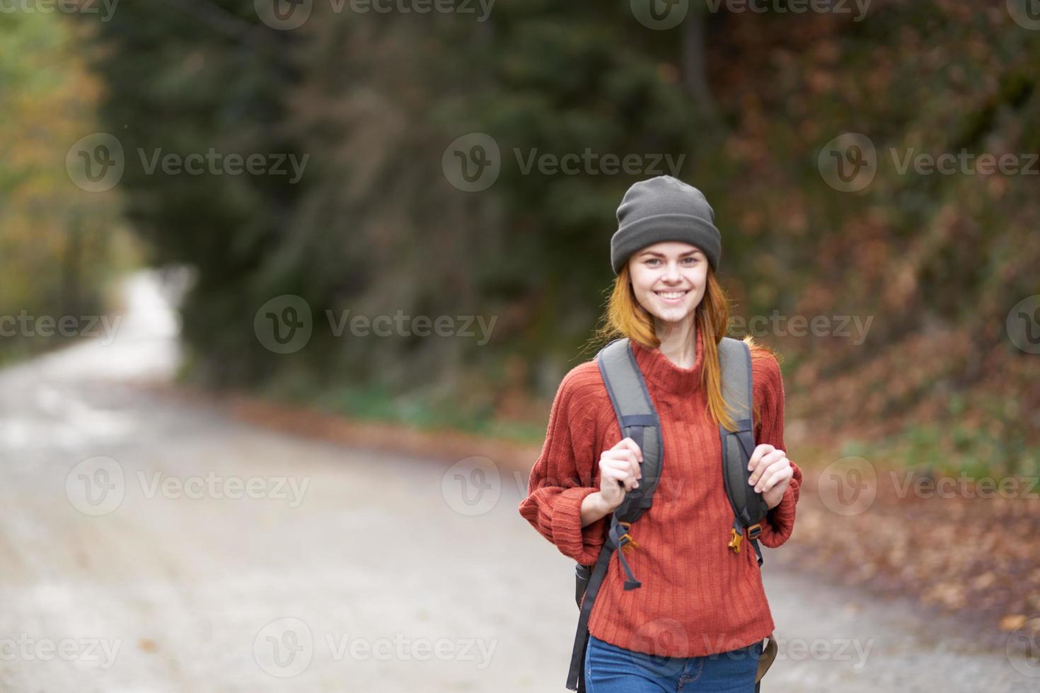 woman with a backpack in full growth walks along the road in the forest in autumn photo