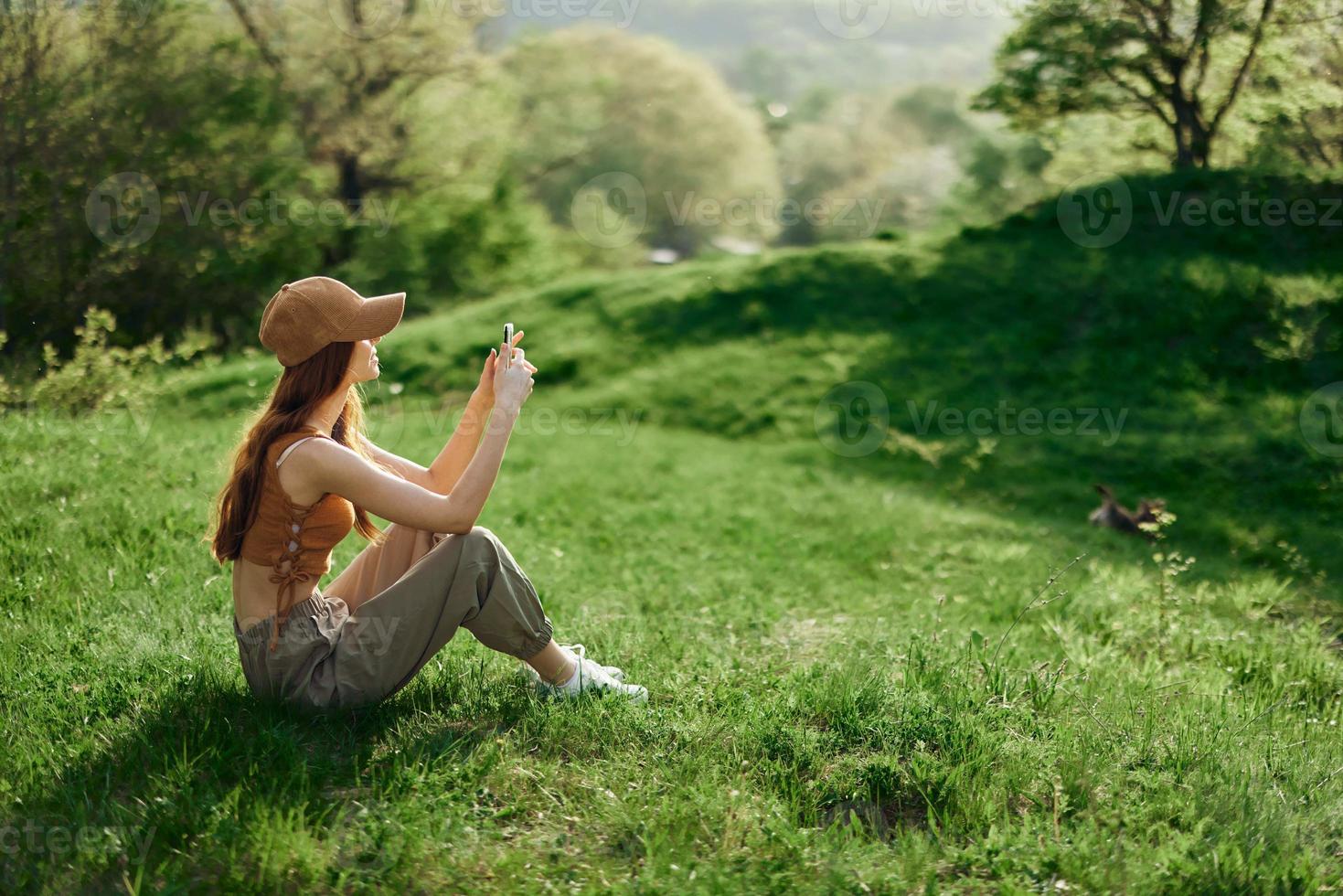 A woman sitting on the green grass in a park in summer against a landscape of trees, the work of a freelancer and blogger photo