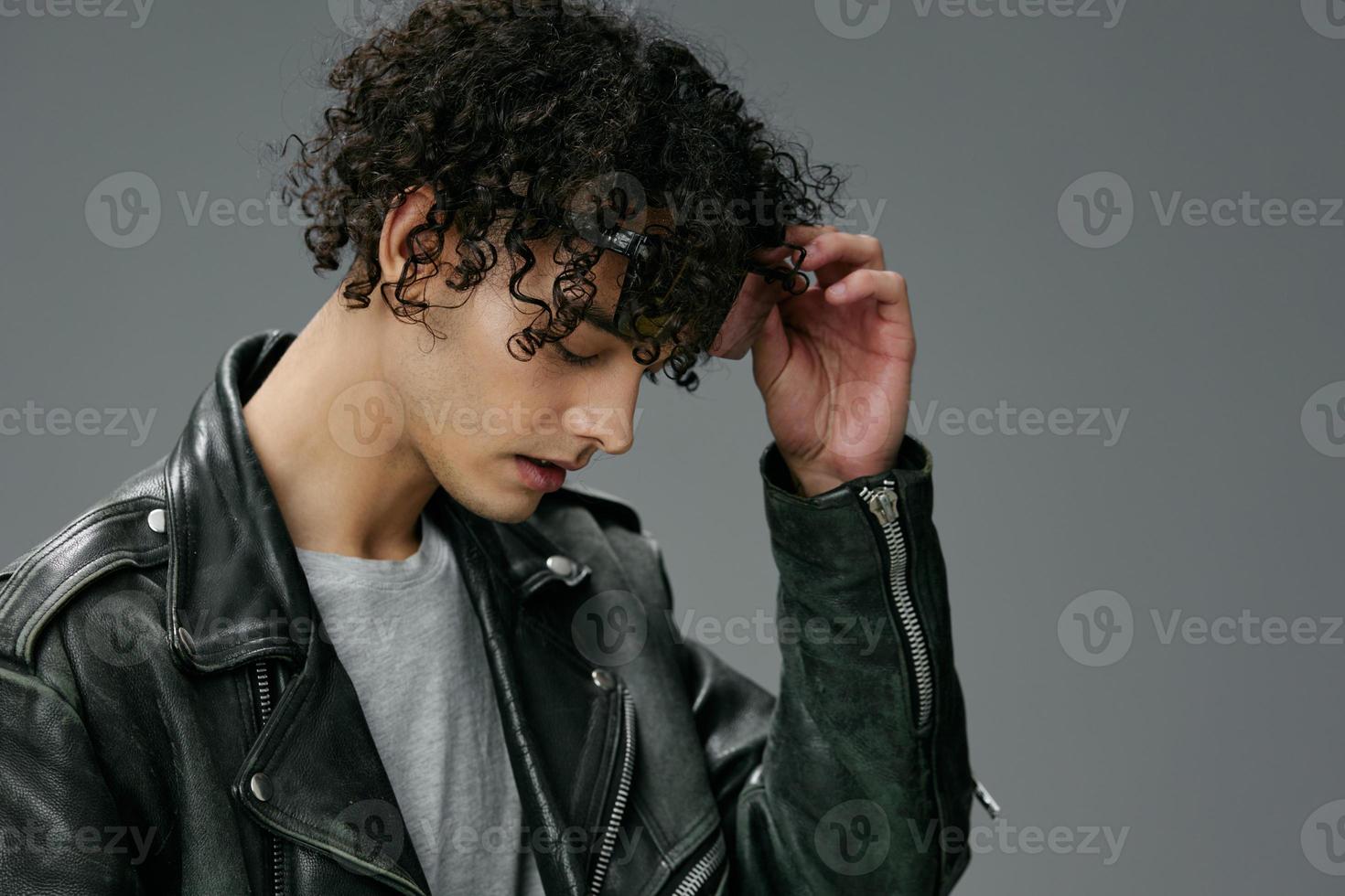 Side of view portrait of stylish tanned curly man leather jacket wear glasses posing isolated on over gray background. Cool fashion offer. Huge Seasonal Sale New Collection concept. Copy space for ad photo