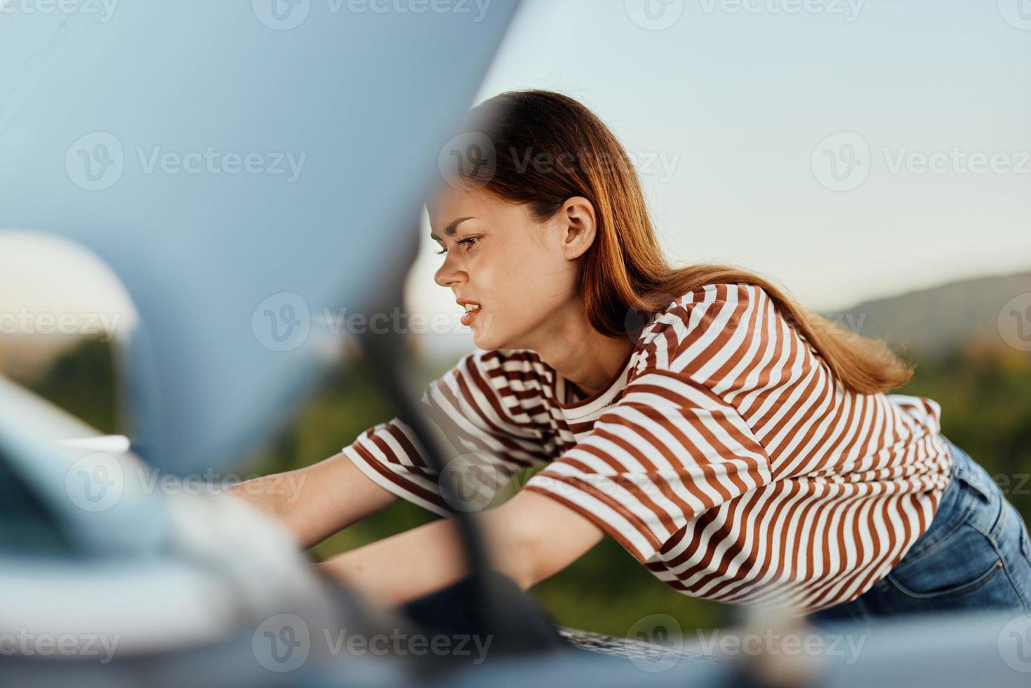 A sad woman looks in disbelief at her broken down car on the road while traveling and does not know what to do photo