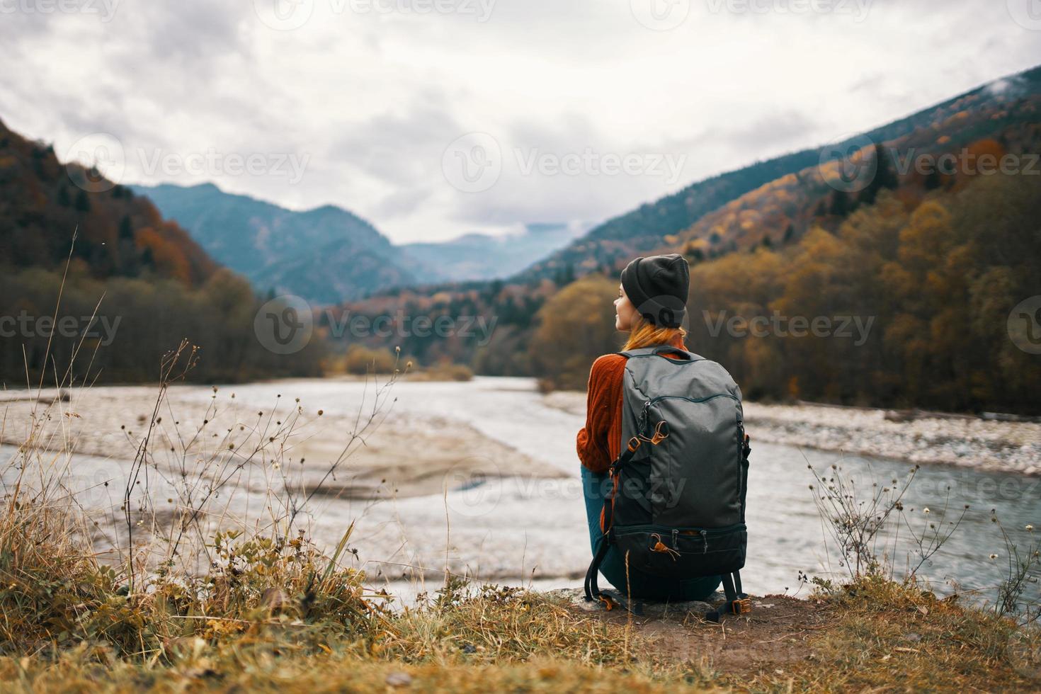 woman traveler with a backpack on her back gestures with her hands and looks at the mountains in the distance photo