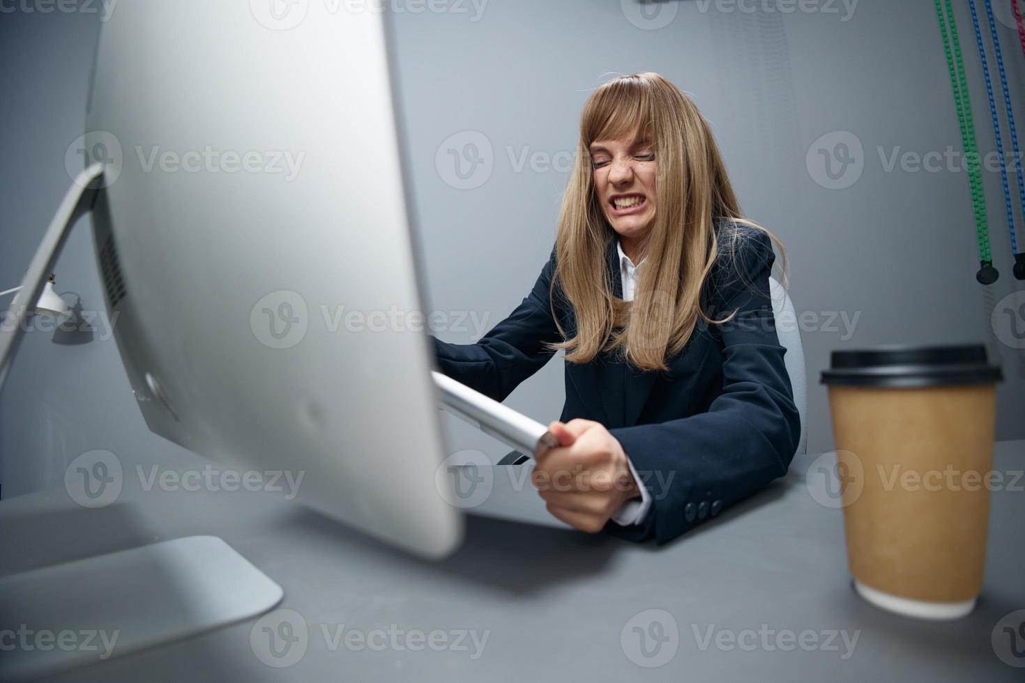 Evil irritated millennial blonde businesswoman worker in blue jacket breaks keyboard hate operation crash in gray modern office. Remote Job, Technology And Career Profession Concept. Wide angle photo