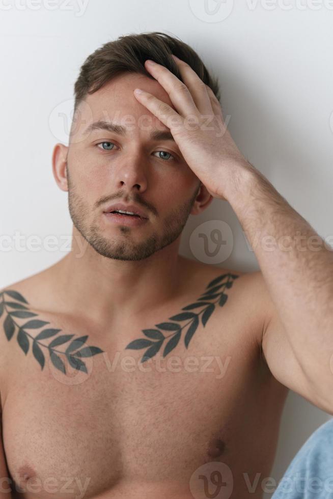 modelado instantáneas de cerca retrato de atractivo desnudo hermoso hombre en pantalones toque frente sentado en piso posando en blanco estudio antecedentes. Moda hombres disparar concepto. Copiar espacio. frio oferta foto