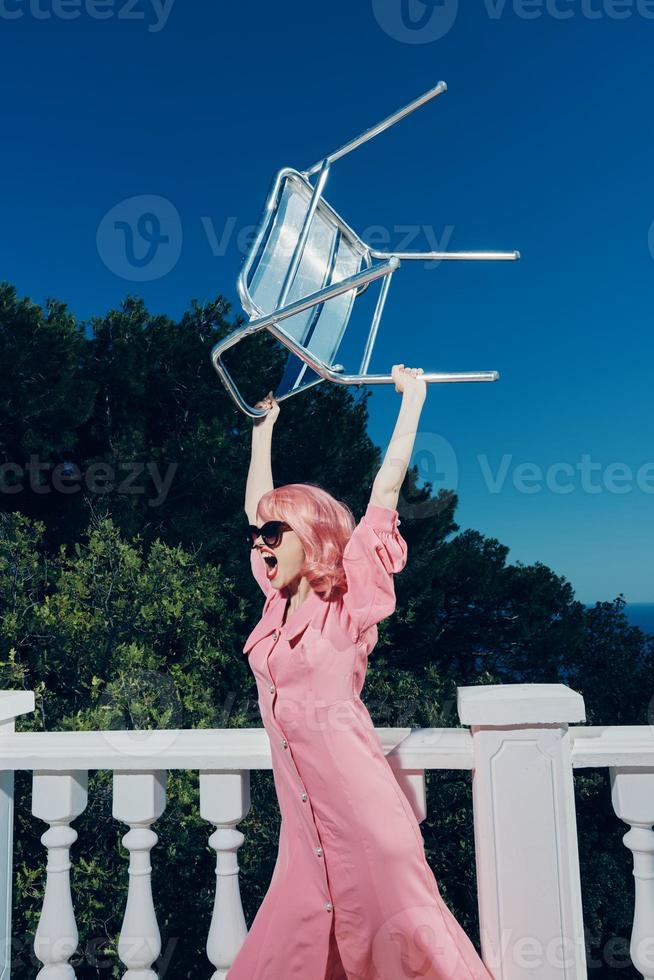 emotional woman with pink hair holding a chair in her hands photo