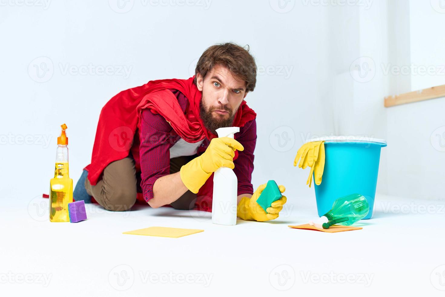 un hombre con limpieza suministros en un rojo impermeable en el piso de un hogar interior profesional foto