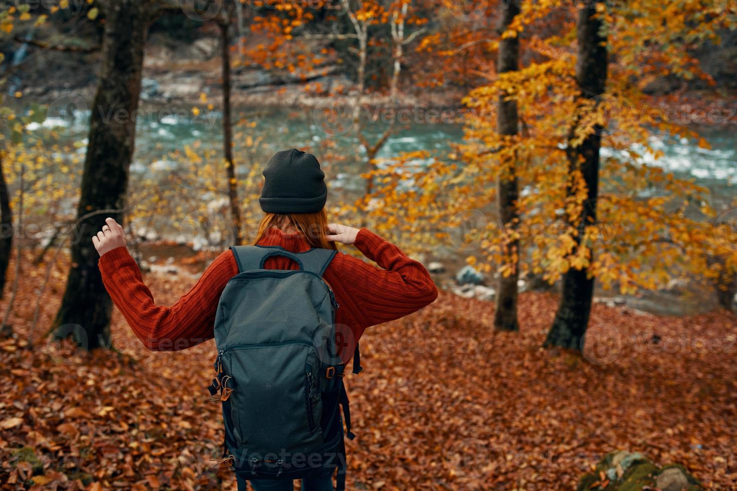 woman in a sweater with a backpack and in jeans walks through the autumn forest in the mountains near the river photo
