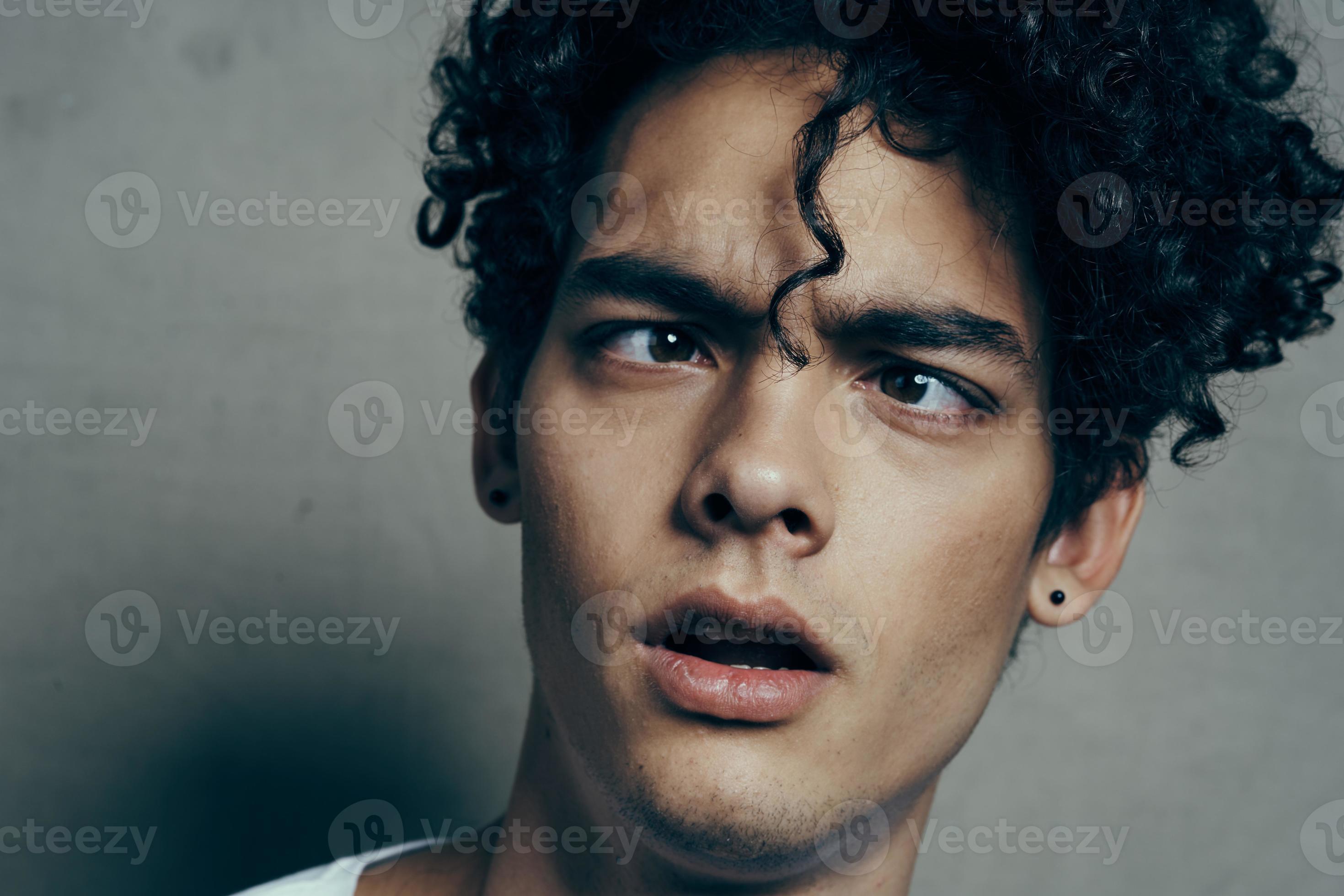 portrait of a handsome guy with curly hair on a gray background white t