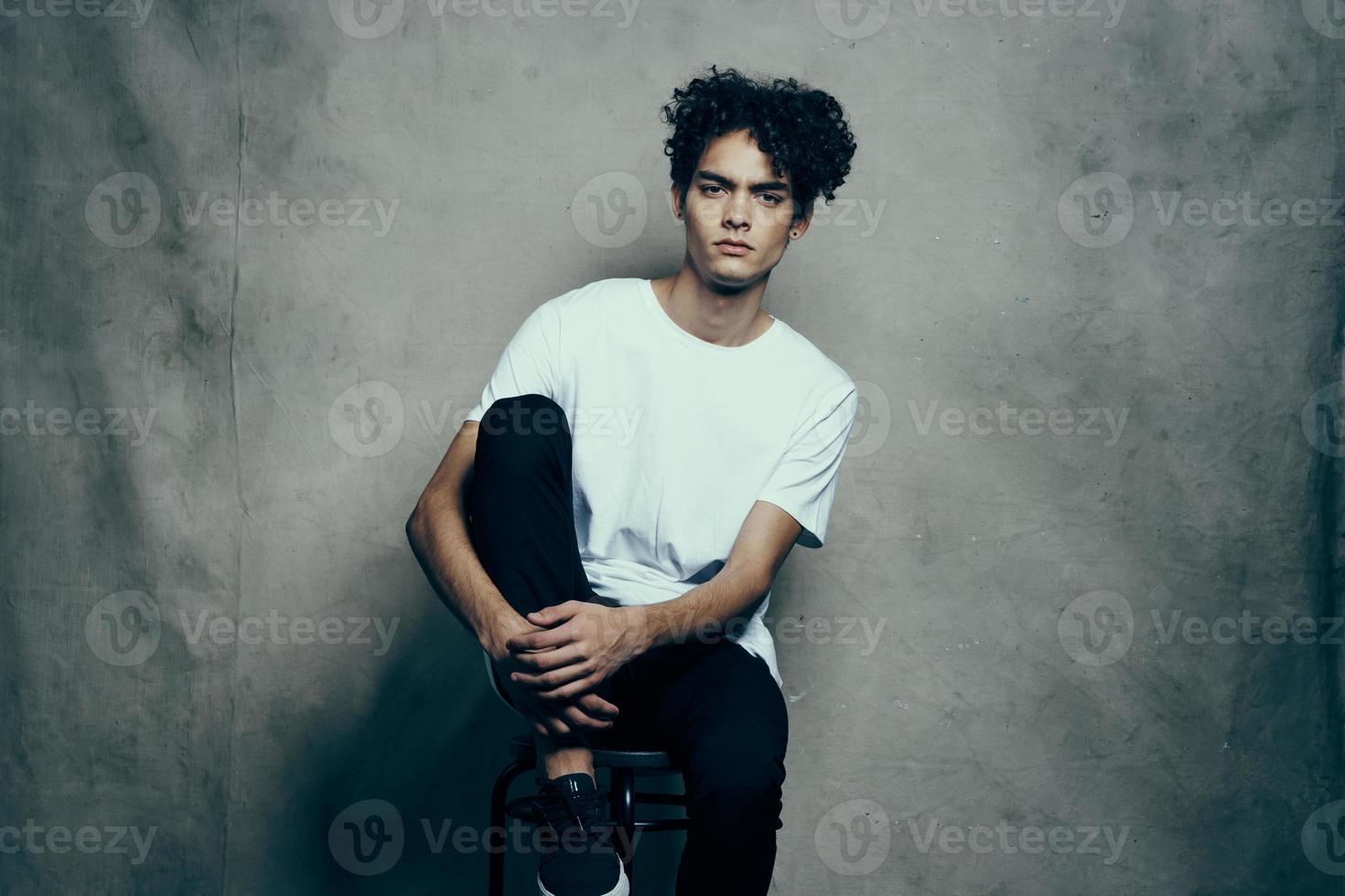 man with curly hair sitting on a chair fashion studio photo