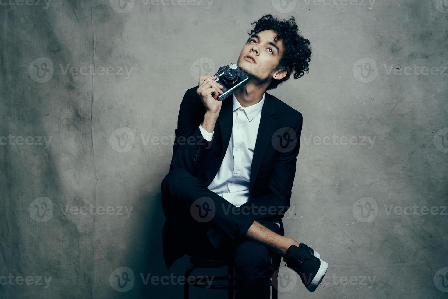 man in trousers in sneakers t-shirt holding a camera in his hand indoors photo