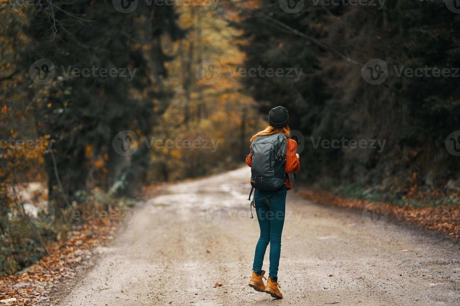 happy traveler with backpack walks on the road in autumn forest photo