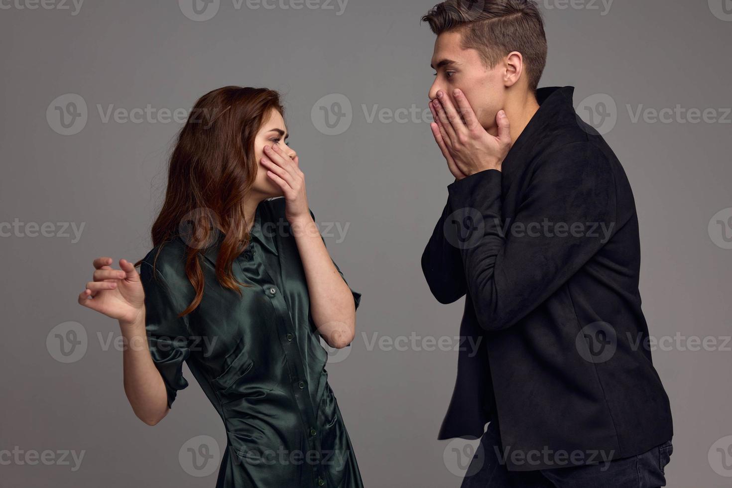 A frightened woman and a surprised man look at each other against a gray background photo