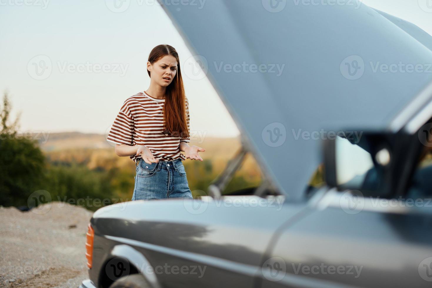 Woman traveler standing near the car with the hood open and looking for the cause of the car breakdown alone without men on the road in the countryside photo