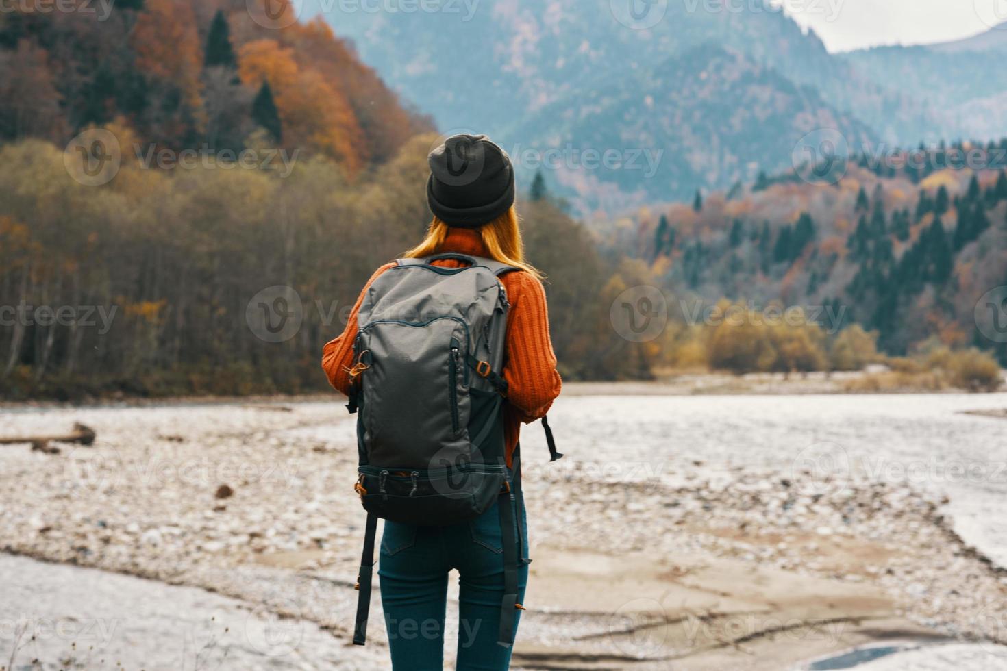 woman travels in the mountains in autumn near the river in nature with a backpack back view photo