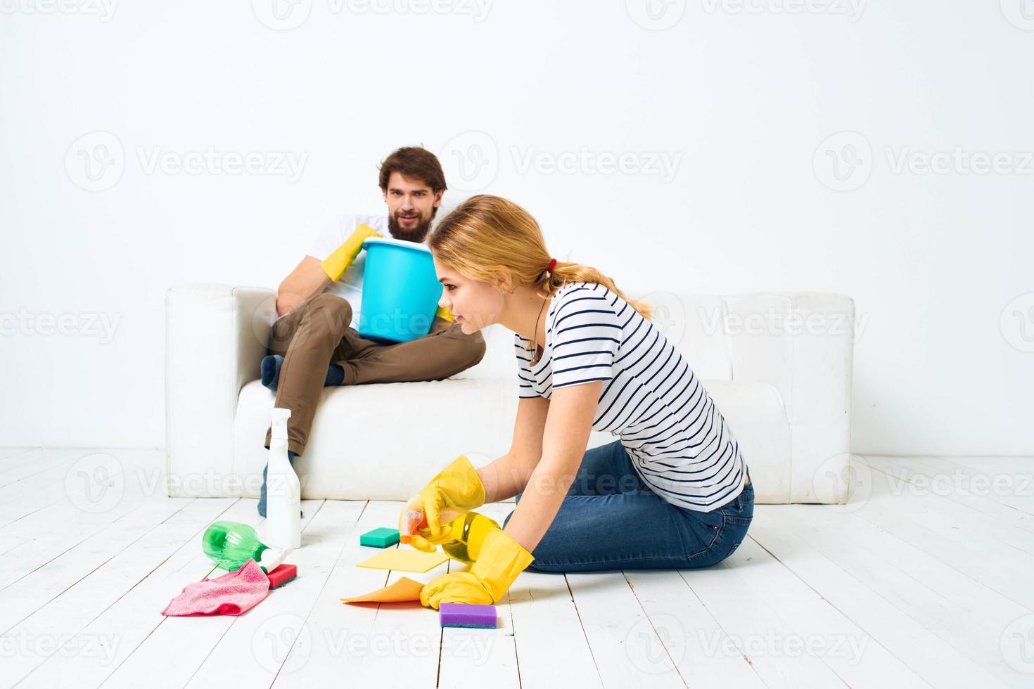 A man sits on a sofa with a bucket of a woman on the floor with a detergent for kitchen interior chores photo