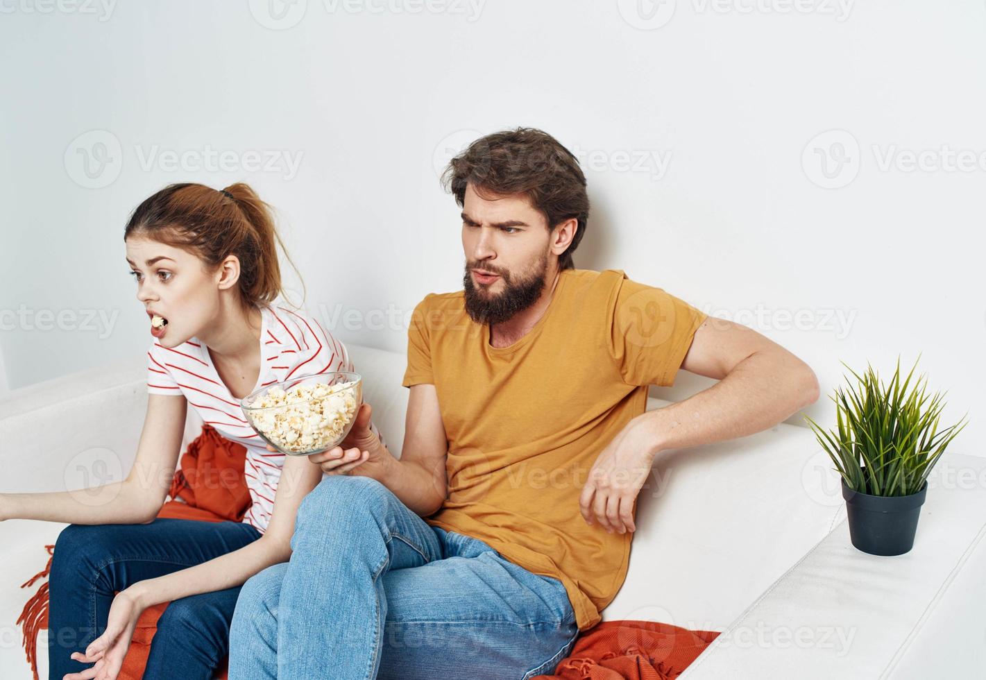 A man and a woman on the couch watching TV with popcorn in a plate photo