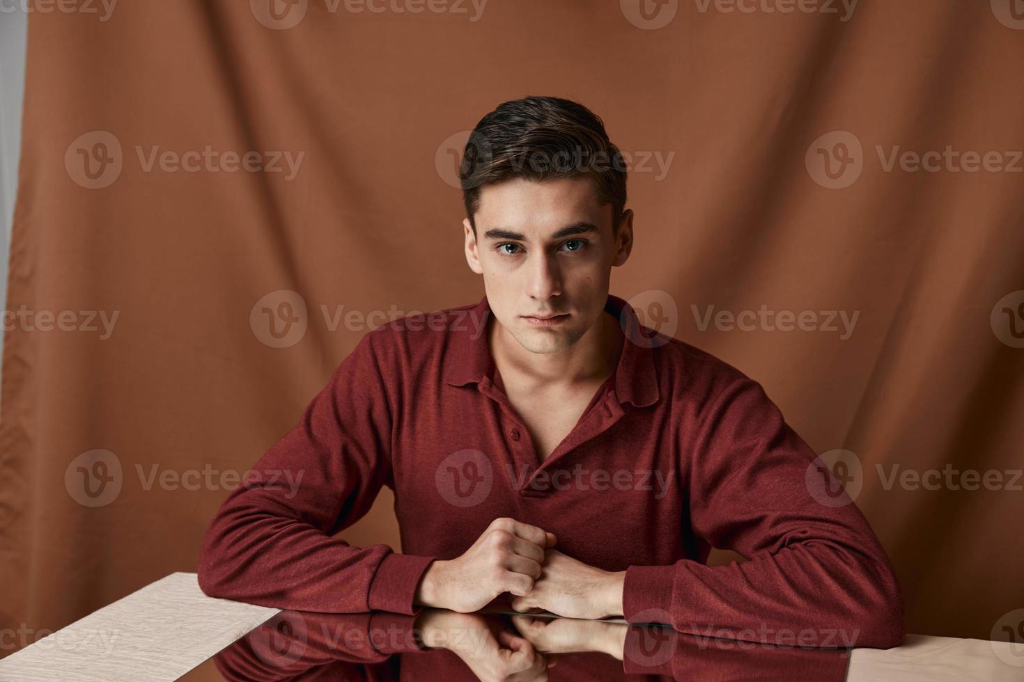 A man on a cloth background with folds sits at a table with a mirror photo