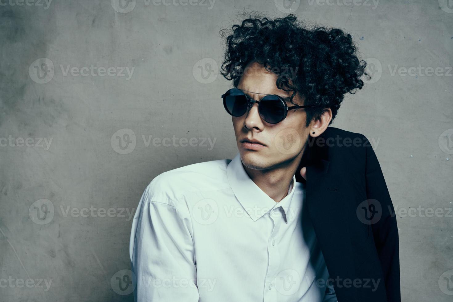 portrait of a curly-haired guy in a shirt with a jacket on his shoulder and glasses on his face photo