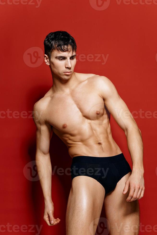 athlete with a naked torso on a red background bent over to the side and pumped up muscles photo