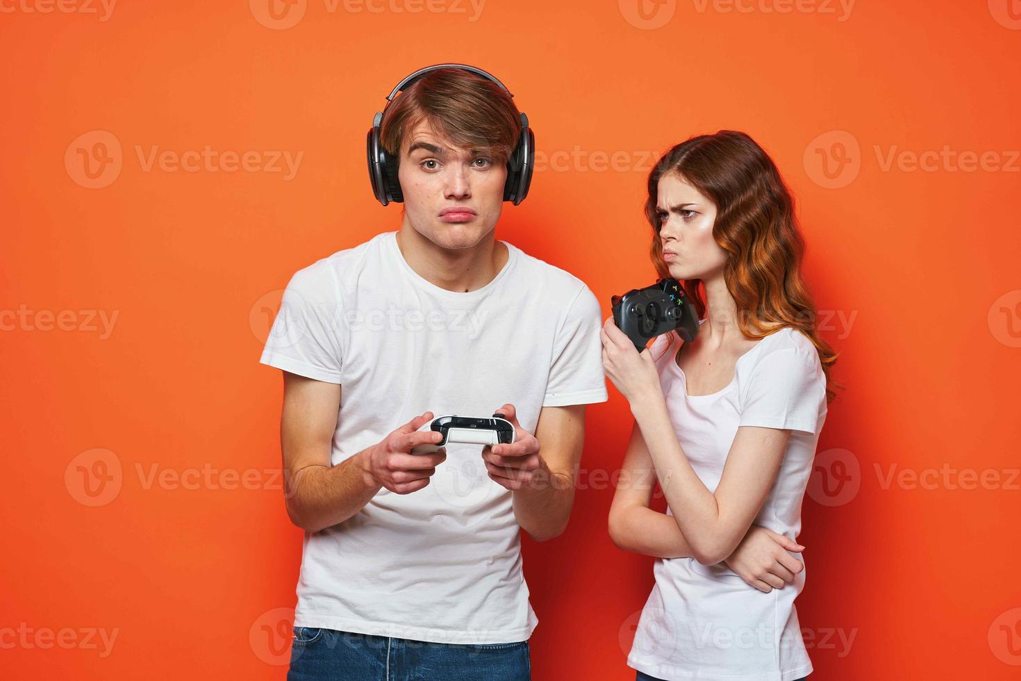 joven Pareja en blanco camisetas con palancas de mando en manos jugando juego amistad naranja antecedentes foto