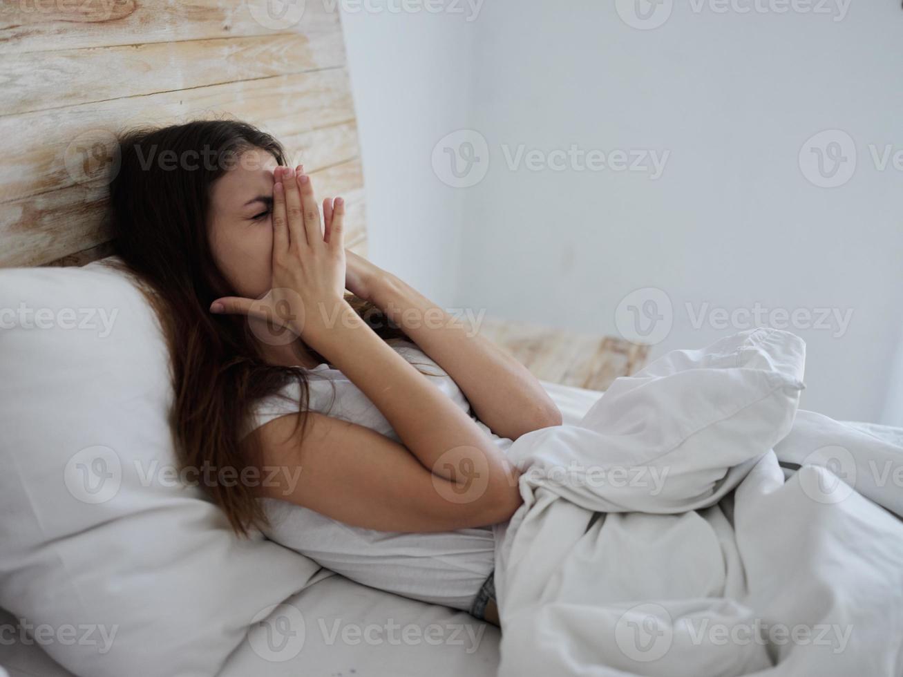 woman with a cold lies in bed hands on face emotions health problems photo