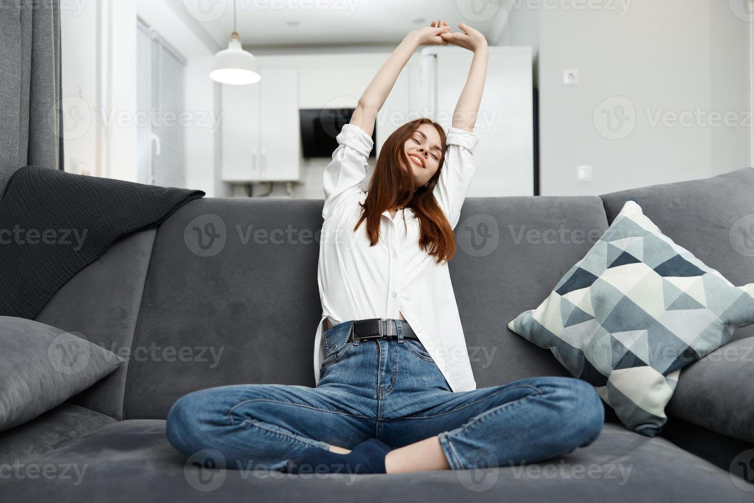 woman pulls herself up holding her hands above her head On the couch at home rest photo