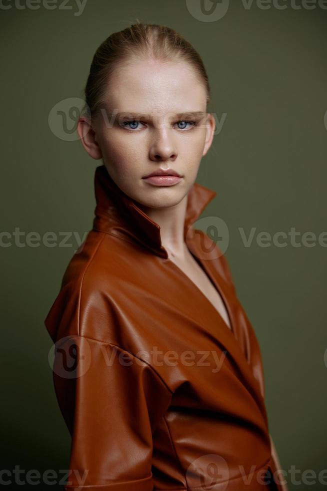 Elegant fashionable young blonde girl with blue eyes with evening makeup in a leather dress looks at the camera posing isolated for banner design. Studio portrait on a green background. Makeup concept photo