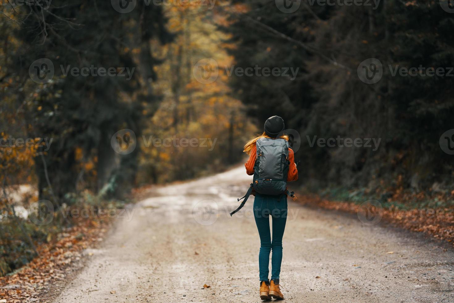 happy woman hiker with backpack walks on the road in autumn forest photo