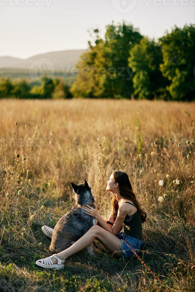 Woman sitting in field with dachshund dog smiling while spending time in nature with friend dog in autumn at sunset while traveling photo