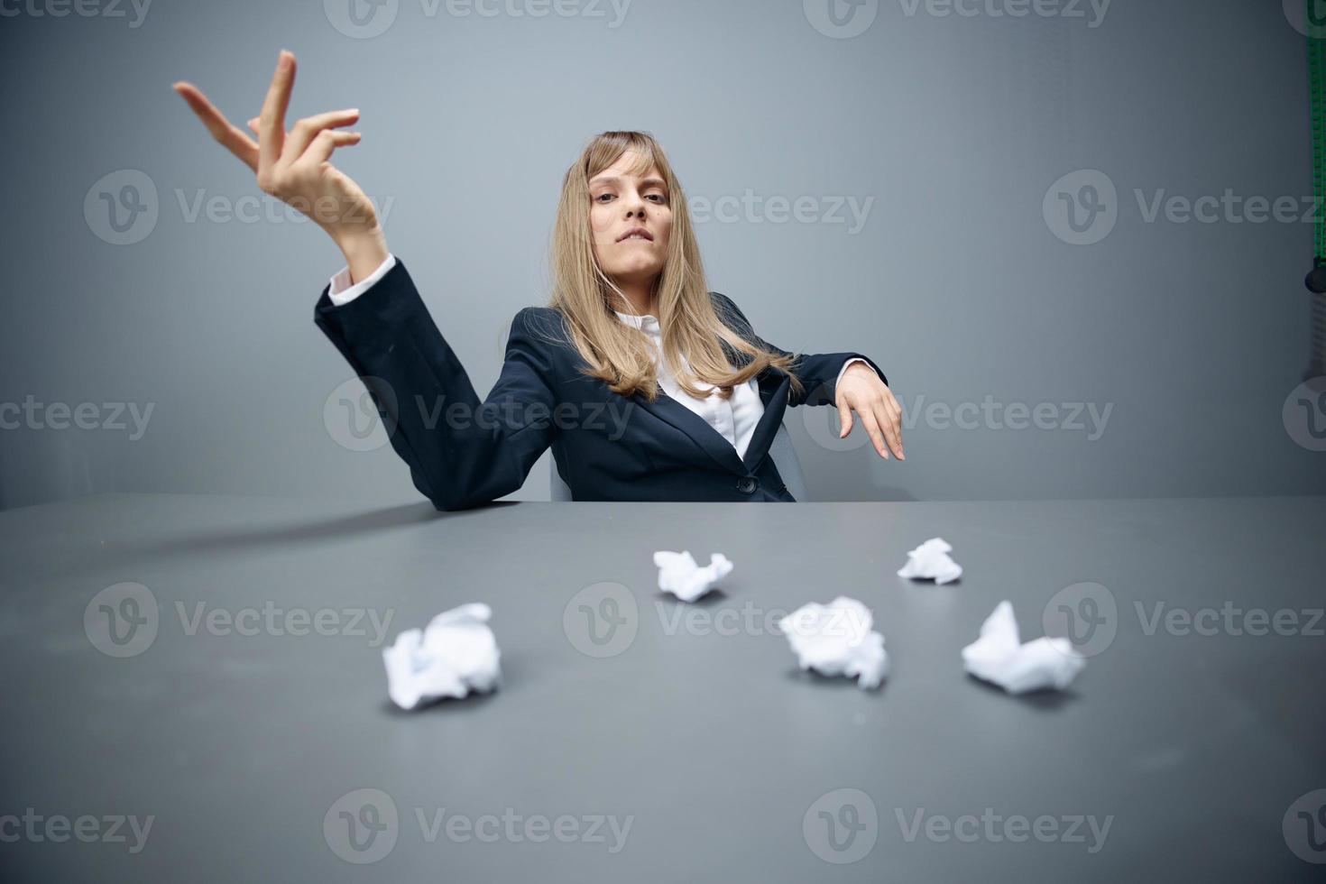 Pretty millennial blonde businesswoman worker in blue jacket throws papers into the camera sitting at workplace in gray modern office. Big boss Concept. Copy space, wide angle photo